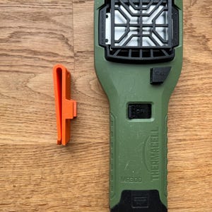 Puede incluir: Dispositivo repelente de mosquitos Thermacell MR300 verde con un bot&oacute;n de inicio negro y una rejilla negra. El dispositivo tiene un clip de cintur&oacute;n negro y naranja.