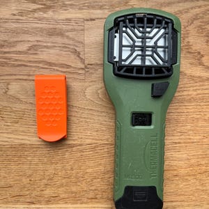 Puede incluir: Un dispositivo repelente de mosquitos Thermacell MR300 verde con un clip negro y un filtro blanco. El dispositivo tiene un bot&oacute;n negro etiquetado como "Start" y un bot&oacute;n negro etiquetado como "Off".