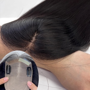 May include: A close-up of a black hair topper with a natural-looking part. The hair is long and straight, with a slight sheen. The topper has clips for easy attachment and is designed to blend seamlessly with natural hair.
