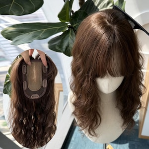 May include: A brown hair topper with wavy texture and bangs is displayed on a mannequin head. The topper is shown both on the head and separately, revealing the clips for attachment. The hair color is a medium brown.