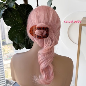 Puede incluir: Una pinza para el pelo de forma ovalada con un patrón de carey marrón que sujeta una sección de cabello rosa pastel peinado en un recogido informal. El texto Casual Updo es visible en letras rosas en el lado derecho de la imagen.