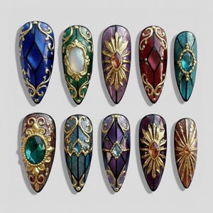 May include: Ten elaborately decorated nail art designs in jewel tones. Each nail showcases a distinct design with gold detailing, featuring geometric patterns, sunbursts, and jewel-like embellishments in blue, green, purple, and red.