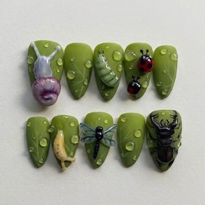 May include: A set of ten almond-shaped press-on nails featuring a matte green leaf pattern with raised 3D dew drops. The designs include a snail, a green caterpillar, two ladybugs, a yellow slug, a blue dragonfly, and a black stag beetle.