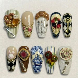 May include: A collection of ten intricately designed nail art creations. Each nail features unique miniature designs, including a pretzel with beer, floral patterns, cutlery, berries, a key, a bunny, a ship, tomatoes, and a teacup. The nails showcase a variety of colors and textures.