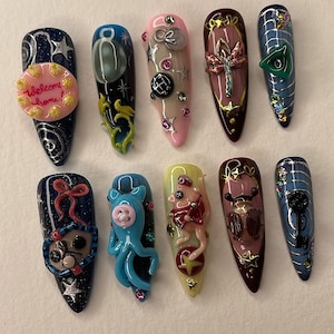 May include: Ten long, almond-shaped acrylic nails, each with a unique 3D design. The nail art includes a welcome home cake, a blue octopus, a pig in a red outfit, and other whimsical elements. The nails feature a variety of colours and textures.