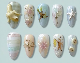 Peut inclure: Dix ongles en forme d'amande présentent des motifs variés. On y trouve une banane en 3D, des motifs floraux, un singe avec une banane, des ballons, une étoile de mer, des rayures, une libellule et des tranches de fruits. Les ongles sont peints dans des couleurs pastel.