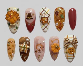 Op de afbeelding: Een set van tien kunstnagels met een herfstthema. Ontwerpen omvatten een kalkoen, een pelgrimshoed, een koffiekopje, herfstbladeren en een effen bordeauxrode nagel. Andere nagels tonen een ster, een eekhoorn en een pompoen.