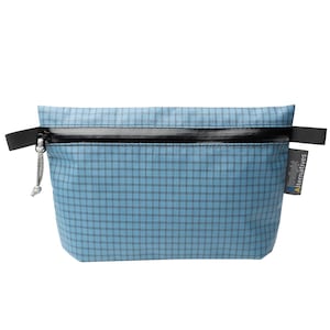 May include: A light blue zippered pouch featuring a dark grid pattern. The pouch has a black horizontal zipper, black side tabs, and a grey cord pull. A small grey tag on the right side displays the text Ultralight Alternatives in white and yellow.