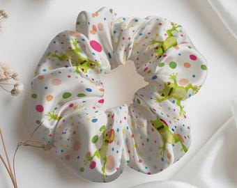 Könnte beinhalten: Weißes Haargummi mit einem verspielten Frosch- und Tupfenmuster. Das Haargummi zeigt grüne Frösche und bunte Punkte auf weißem Hintergrund. Ein stilvolles Haaraccessoire für den Alltag.