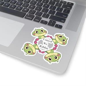 May include: A sticker featuring four cartoon frogs in a circular arrangement, each holding a section of a white, geometric shape. The shape contains the text "United We Ribbit". The frogs are green with pink accents and large, friendly eyes.