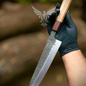 May include: A kitchen knife with a hammered, textured steel blade and a two-toned wooden handle. The handle features a lighter wood section near the pommel and a darker wood bolster near the blade. The blade has a sharp, pointed tip.