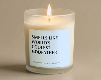 May include: A lit, glass candle with a white label that reads "Smells Like World's Coolest Godfather." The candle has a light beige wax and a visible wick. The candle is in a clear glass container.