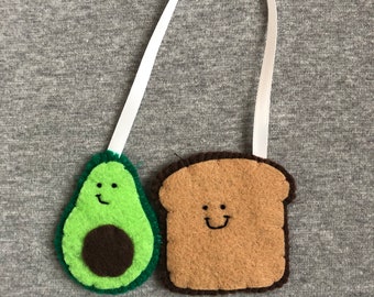 May include: A white ribbon bookmark with a green felt avocado and a brown felt toast, both with smiling faces.