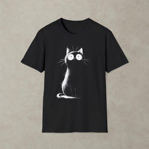 Könnte beinhalten: Schwarzes T-Shirt mit einer Illustration einer schwarzen Katze mit großen, runden Augen. Die Katze ist sitzend dargestellt, mit weißen Details, die sich vom dunklen Hintergrund abheben. Ein einfaches, ausdrucksstarkes Design für Katzenliebhaber.