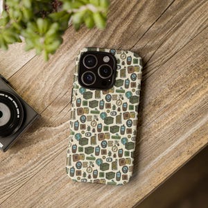May include: A phone case with a cream background and a repeating pattern of travel-themed illustrations in green, brown, and blue. The design includes compasses, globes, bugs, and other travel-related icons. The case is on a wooden surface.