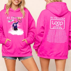 May include: Bright pink Ed Sheeran hoodie. The front displays a graphic of a performer and the text "AUSTRALIA 2026" and "91". The back features "Ed Sheeran Loop tour" and a list of tour dates and locations.