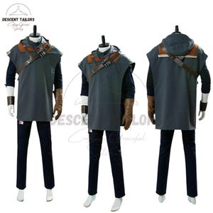 Puede incluir: Un disfraz gris con capucha y detalles en cuero marrón, incluyendo una correa para el hombro y puños. El disfraz se muestra en un maniquí con pantalones azul marino y guantes marrones. El texto "DESCENT TAILORS" es visible.