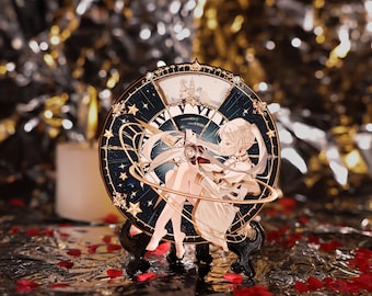 May include: A decorative clock featuring a celestial design with a cartoon character. The clock face is dark blue with gold accents, stars, and Roman numerals. The character is depicted in a white dress. The clock is displayed on a black stand.