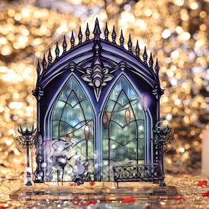 May include: A detailed, transparent acrylic art piece depicting a gothic-style arched window with a bench and two figures. The artwork features shades of blue and purple, with decorative elements and a detailed design. The background is blurred with golden bokeh.