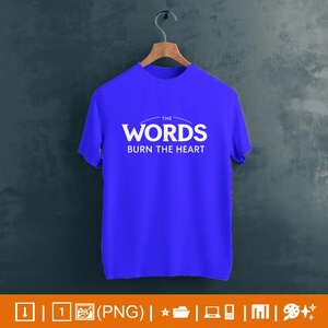 May include: A vibrant blue t-shirt featuring the white text "THE WORDS BURN THE HEART". The tee is suspended from a wooden hanger. The text is centrally positioned. The background is a dark, muted tone.