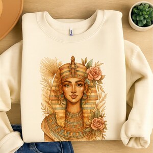 May include: Cream sweatshirt with a watercolour illustration of an Egyptian pharaoh. The artwork features a detailed portrait with a headdress, jewellery, and floral accents. The design is centred on the front of the garment.