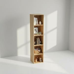 以下が含まれることがあります： 5段の棚がある、明るい色の木製本棚。本、装飾品、小さなバスケットが棚に置かれています。本棚は白い壁の前に置かれ、ミニマリストな美学を作り出しています。高さは約180cmです。