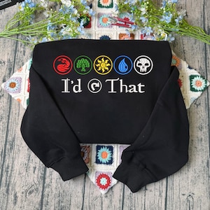 May include: A black long-sleeve sweatshirt featuring a graphic print of five colored circular icons representing fire, forest, sun, water, and a skull. Below the icons, the white text reads I'd (tap symbol) That in a stylized font.