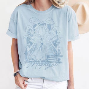 Pu&ograve; includere: T-shirt azzurra con grafica a tema Cenerentola. Il design include un orologio, una scala e la scritta "Meet me at Midnight". La maglietta ha maniche corte e una vestibilit&agrave; ampia.