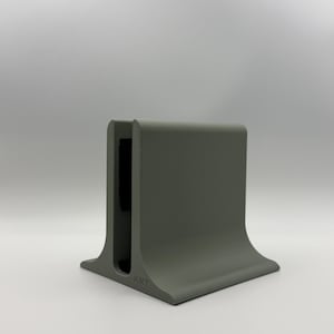 Peut inclure: Un support de bureau gris mat doté d'une base large et évasée ainsi qu'une fente verticale centrale pour maintenir des objets. Le support présente un profil lisse et incurvé avec les lettres KMT gravées en petit sur le coin avant inférieur.