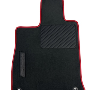 May include: Black car floor mat with a red trim. The mat has a quilted black section and two metal grommets. The mat is designed to fit the driver's side of a vehicle.