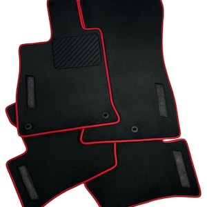 May include: Set of black car floor mats with red trim. The mats have a textured area for the driver's feet and are designed to fit a vehicle's interior. The mats are made of a durable material.