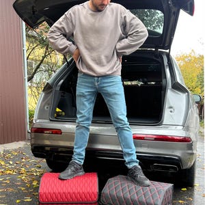 May include: Two car trunk organizers with a diamond-stitched pattern. One is red with black trim, and the other is black with red trim. The text "STURDY FRAME" is at the bottom of the image. A person is standing on top of the organizers.