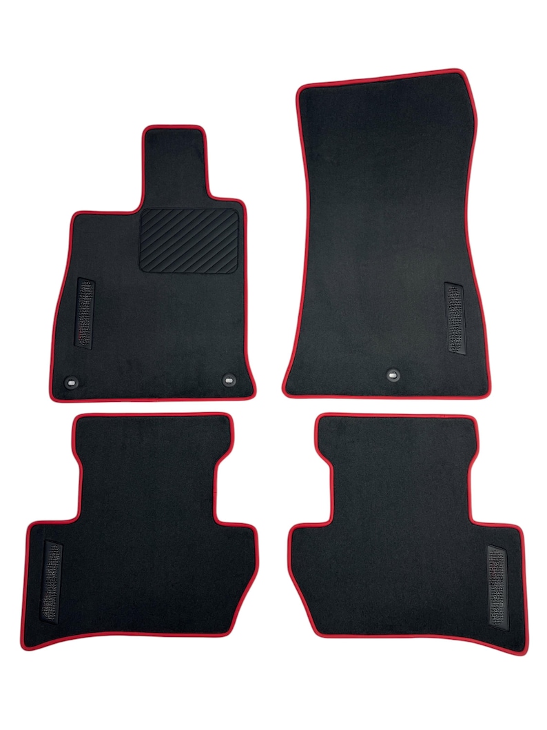 May include: Set of four black car floor mats with red trim. The mats have a textured surface and are designed to fit a vehicle's interior. The set includes two front and two rear mats.