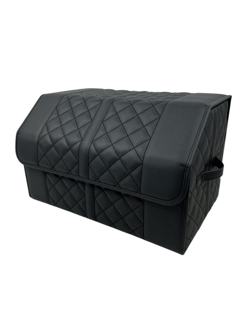 May include: Black car trunk organizer with a quilted diamond pattern. The organizer has a rectangular shape with a hinged lid and a handle on the side. The interior is not visible.