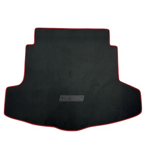 May include: Black car trunk mat with a red trim. The mat has a rectangular shape with a contoured design to fit the trunk. A rectangular textured patch is centered on the mat.