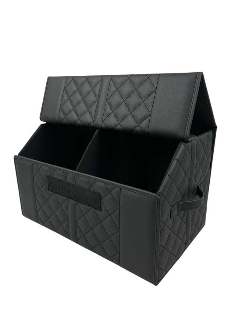 May include: Black, quilted car organizer with two compartments and a lid. The organizer has a rectangular shape with a diamond pattern and a handle on the side. A velcro strap is on the front.