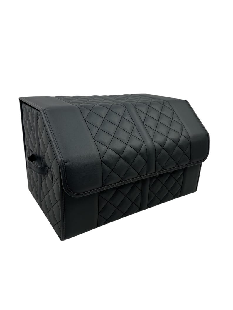 May include: A black, quilted, rectangular storage container with a hinged lid. The container features a diamond pattern and a handle on the side. The material appears to be leather or a leather-like material.