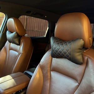 May include: Brown leather car seats with black headrest pillows. The headrest pillows have a diamond-stitched pattern with orange stitching. The car's interior has a brown and black color scheme.