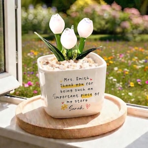 Puede incluir: Una maceta de cer&aacute;mica blanca con un arreglo de tulipanes de cristal. La maceta tiene el texto "Sra. Smith, Gracias por ser una parte tan importante de mi historia, Sarah". La maceta est&aacute; sobre una bandeja de madera.