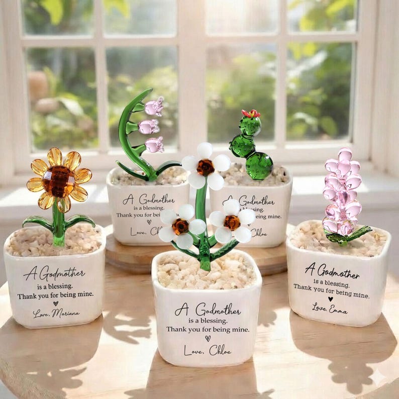 May include: Five glass flower sculptures in white pots, each with a different flower design. The pots have text that reads "A Godmother is a blessing. Thank you for being mine."