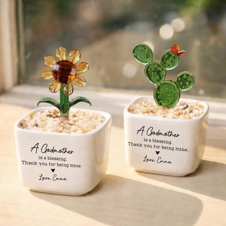 May include: Two small white square planters with decorative glass plants. One features a yellow sunflower, the other a green cactus. Each planter has the text "A Godmother is a blessing. Thank you for being mine. Love, Emma."