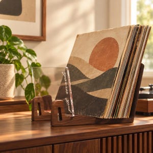 May include: A dark wood vinyl record storage stand holding a collection of records. The stand features a clear acrylic front panel with the text "guith records" printed vertically in white script. The records display a sunset graphic cover.