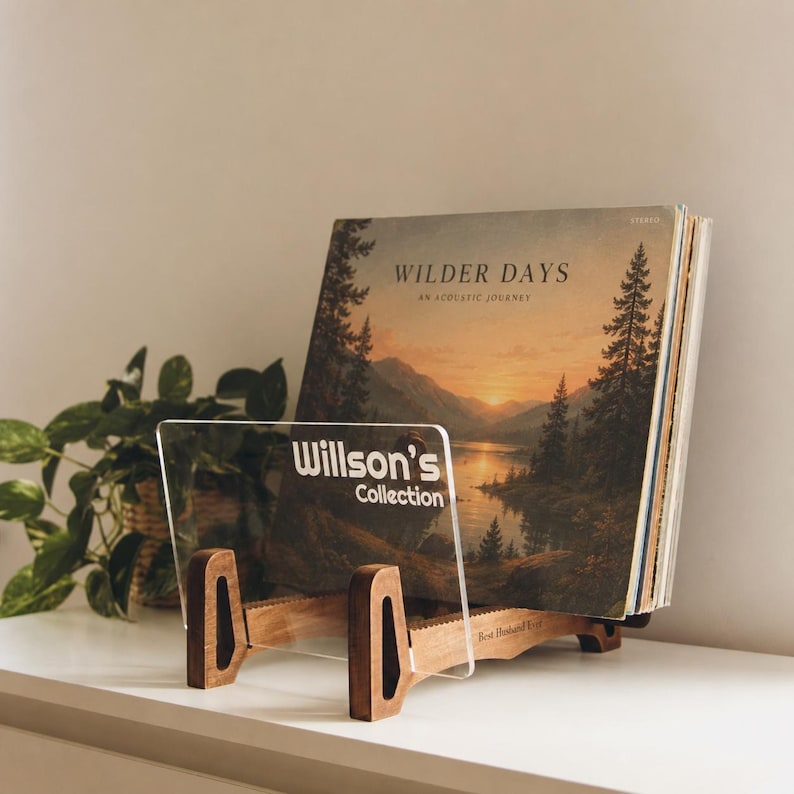May include: A wooden vinyl record display stand with a clear acrylic front panel featuring the white text Willson's Collection. The stand holds a vinyl record sleeve titled Wilder Days An Acoustic Journey, which depicts a sunset over a lake and forest.