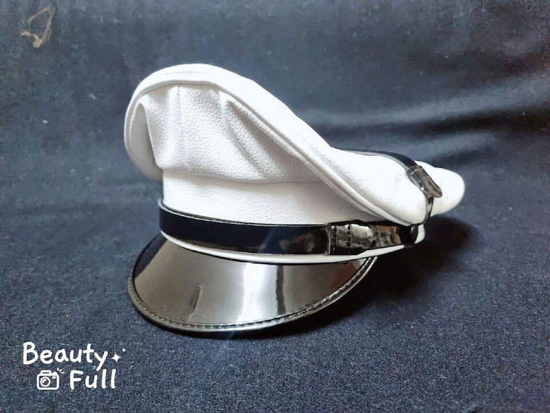 Puede incluir: Una gorra blanca de pico con una banda negra y una visera negra brillante. La gorra tiene una superficie ligeramente texturizada.