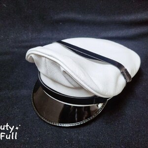 Puede incluir: Un sombrero de cuero blanco con una banda negra y un ala de charol negro.