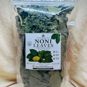 Pode incluir: Uma bolsa de plástico transparente resselável cheia de folhas de noni secas verdes. O rótulo branco apresenta o texto TOPESELLER LTD, NONI LEAVES, DRIED HERBAL LEAVES, MORINDA CITRIFOLIA, 100% NATURAL, PREMIUM QUALITY, CAREFULLY SELECTED e WWW.TOPESELLERHERBS.COM.