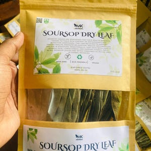 Puede incluir: Una bolsa de papel marrón con una etiqueta blanca que dice "Soursop Dry Leaf" y contiene hojas de guanábana secas. La etiqueta también incluye información sobre el producto, como su estado no-GMO, ecológico y vegano, así como la fecha de caducidad y la cantidad de hojas incluidas.