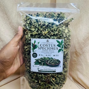 Può includere: Una busta richiudibile in plastica trasparente riempita con foglie di erbe essiccate verdi di Costus speciosus. L'etichetta riporta il testo Costus Speciosus (Thebu Kola), Dried Herbal Leaves e il sito web www.topesellerherbs.com con varie icone.
