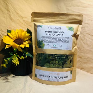 May include: A package of dried Jatropha Curcas leaves, with text that reads "Dried Jatropha Curcas Leaves". The package is brown with a clear window showing the green leaves. A yellow sunflower is to the left of the package.