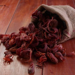 May include: A hessian sack spilling out dried mace blades, which are deep reddish-brown, lacy, and irregular in shape. The spice pieces are scattered across the surface, showcasing their fibrous, delicate, and intricate structure in a natural state.